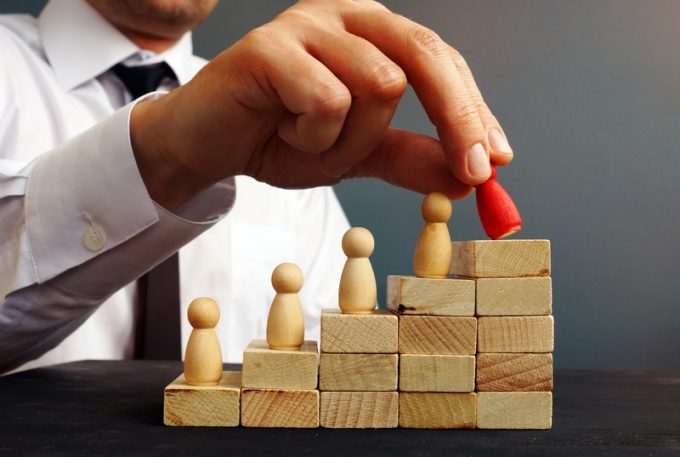 Job Promotion. Manager is holding figurine near career ladder. Worker raises.
